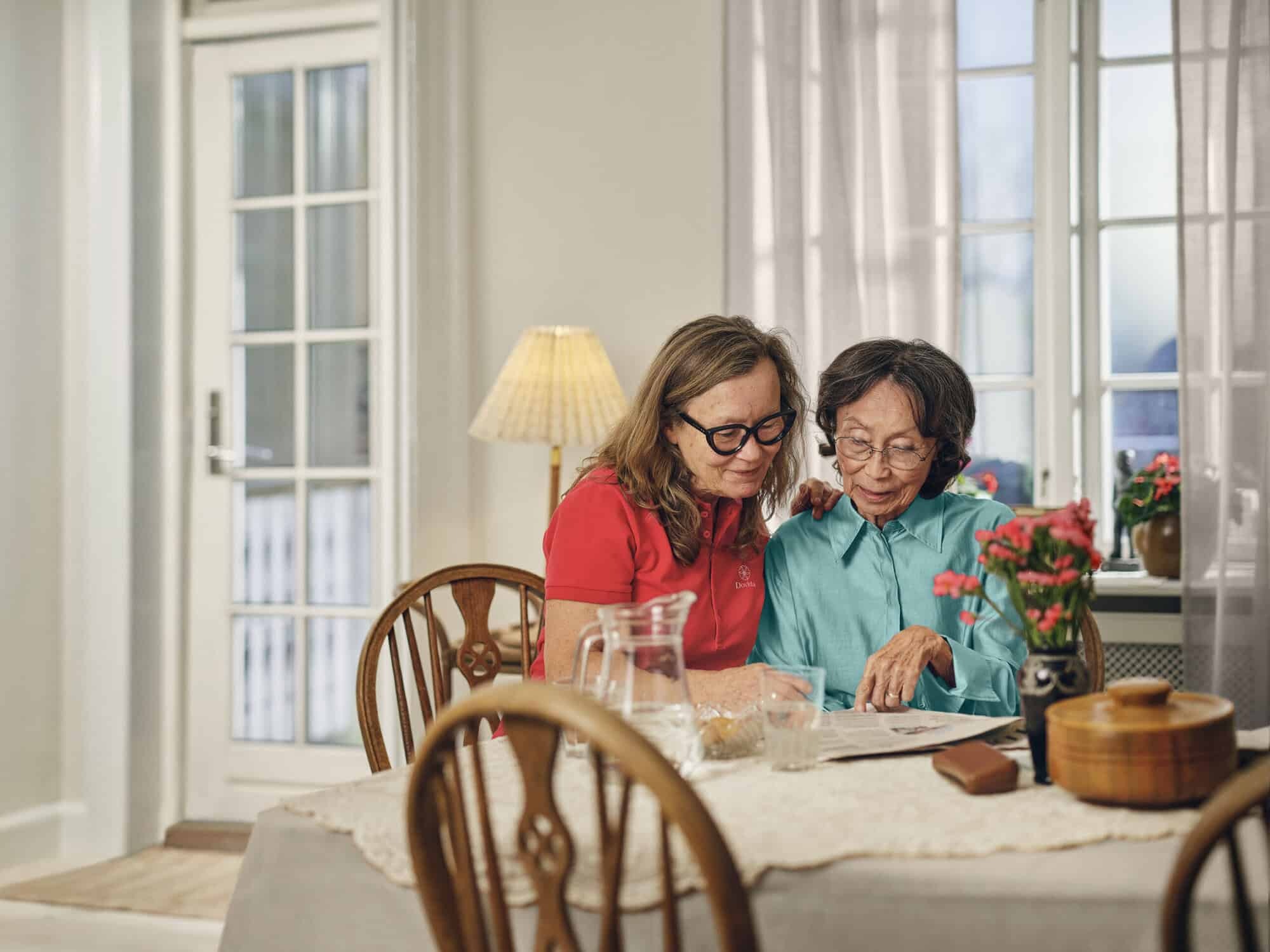 Dovida Caregiver supporting elder with in home care, reading together at a dining table