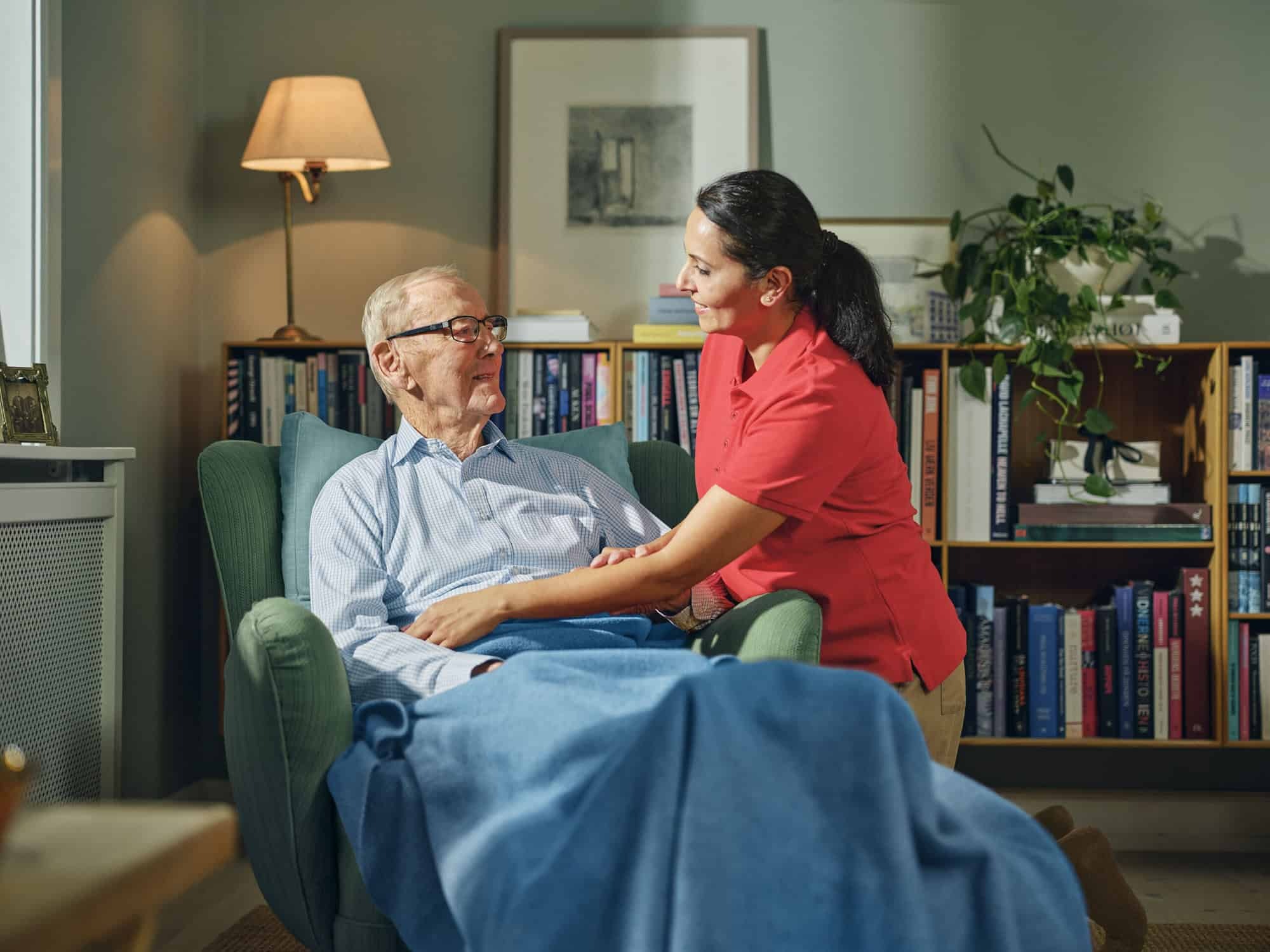 A caregiver supports an elderly man in a chair, reflecting the dedication found in caregiver training and Dovida jobs.